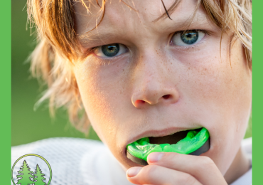 Young athlete putting in a green sports mouthguard, close-up of face with intense expression, wearing white sports gear — promoting custom mouthguards at Spring Hill Dental.