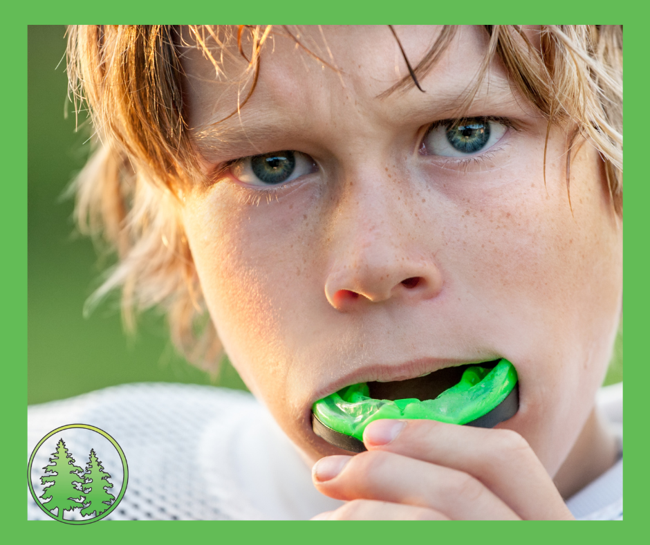 Young athlete putting in a green sports mouthguard, close-up of face with intense expression, wearing white sports gear — promoting custom mouthguards at Spring Hill Dental.